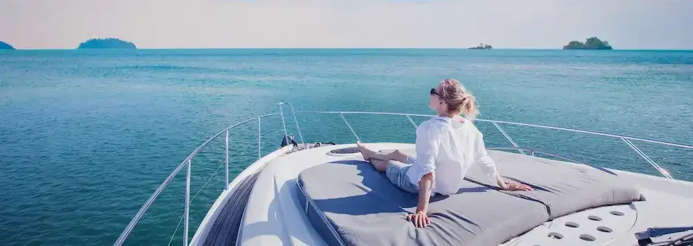 Calming photograph of a young lady relaxing on a luxury yatch in the ocean on a sunny day, the vista is minimal with a scattering of islands in the distance.